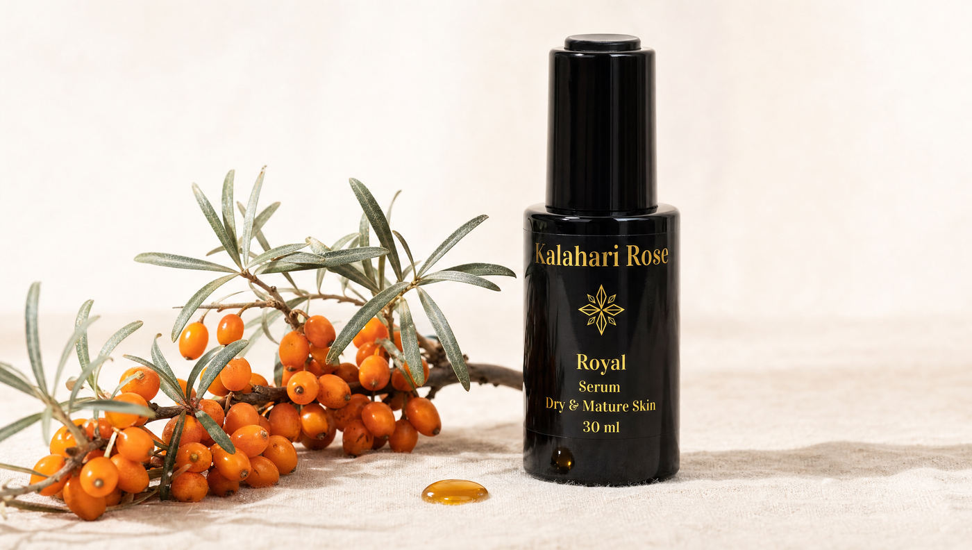 Kalahari Rose Royal Serum on ivory linen with fresh sea buckthorn branch, orange berries, silvery-sage leaves, and an amber oil droplet