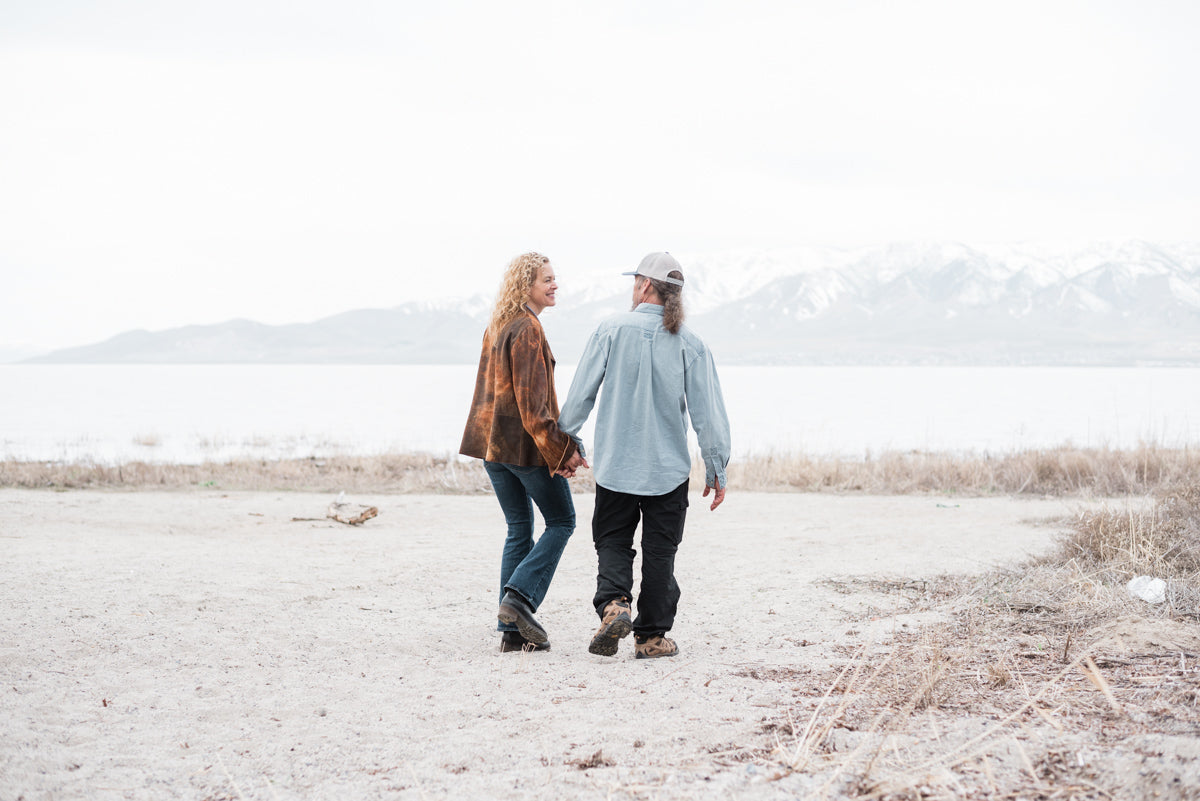 Couple walking hand in hand between lake and mountains